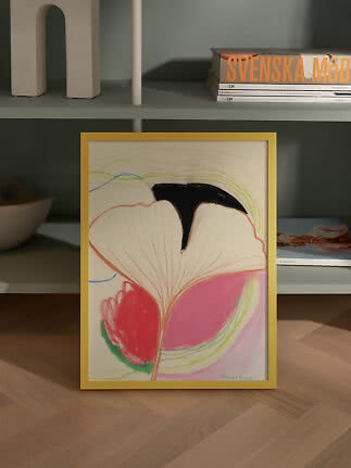 Lámina floral abstracta con marco amarillo apoyada en una estantería gris