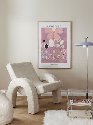 Oprawiony plakat Hilmy af Klint z różowym abstrakcyjnym motywem na beżowej ścianie nad fotelem