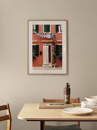 Framed photo of a red facade with green shutters and laundry hanging above a doorway