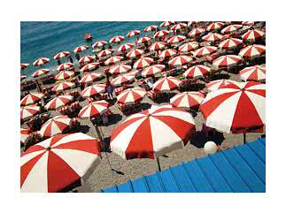 Crowded beach with red and white umbrellas and loungers by the blue sea