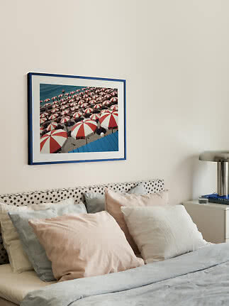 Blue-framed wall art of red and white beach umbrellas above a bed with soft light pillows.