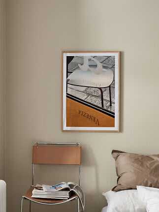 Framed art print with chair motif above a chair and bed in a beige bedroom