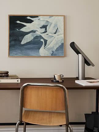 Skrivbord med stol, lampa och inramad målning av vita svanar på ljus vägg