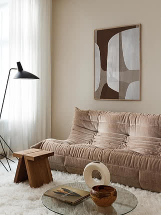 Beige rillet sofa i stue med abstrakt vægkunst, sort gulvlampe og glasbord