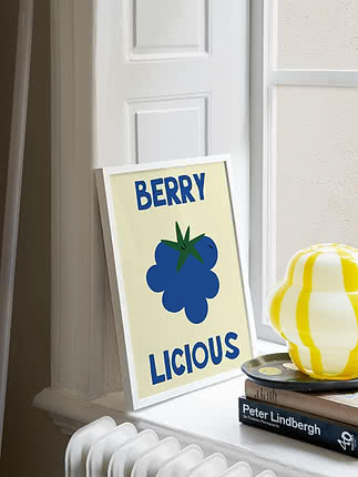 Póster enmarcado con una baya azul y el texto "BERRY LICIOUS" sobre un alféizar blanco.