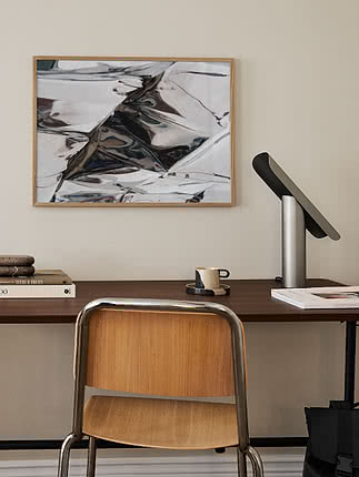Skrivebord med stol, bordlampe og indrammet abstrakt kunst på lys væg