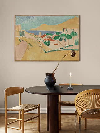 Framed coastal landscape painting above a round dining table with vase and candleholder