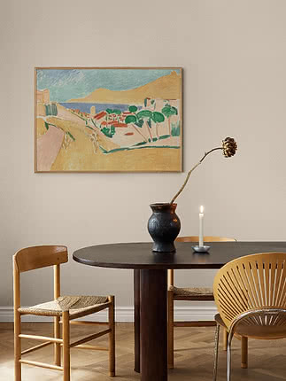 Framed landscape painting with coast, hills and trees hanging above a dark dining table