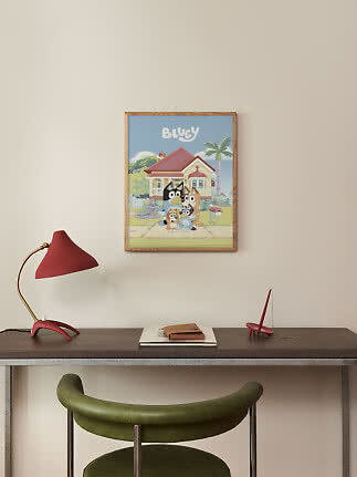 Framed Bluey poster on wall above desk with red lamp and green chair