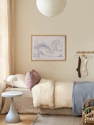 Gemütliches Kinderzimmer mit niedrigem Bett, weißen Kissen, kleiner weißer Lampe und gerahmtem Bild