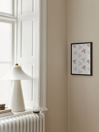 Schwarz gerahmtes Poster mit rosa und grauen Mausmotiven an beigefarbener Wand neben weißer Lampe