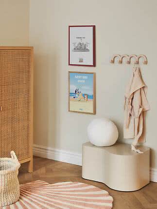 Kids room with beige wall hooks, robe, two posters and a wavy bench.