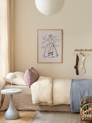Gemütliches Kinderzimmer mit niedrigem Bett, weißer Tischlampe, Kissen, Wandbild und Papierlampe.