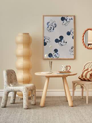 Gerahmtes Mickey- und Minnie-Mouse-Poster an beiger Wand über rundem Holztisch