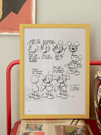 Gerahmtes Schwarz-Weiß-Poster mit Mickey-Mouse-Skizzen in gelbem Rahmen auf einem Tisch