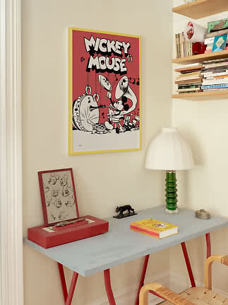 Mickey-Mouse-Poster im gelben Rahmen über grauem Tisch mit grüner Lampe und Büchern