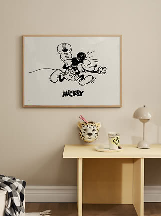 Gerahmtes schwarz-weißes Mickey-Mouse-Poster an beiger Wand über hellem Beistelltisch