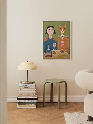 Indrammet kunstplakat på væg med kvinde og kat ved bord med vinglas i lyst, moderne rum