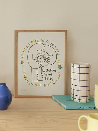 Inramad konstbild med figur och texten "Butterflies in my Belly" på en hylla