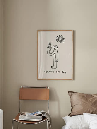 Framed poster with simple line drawing of a figure holding a flower under a sun on a beige wall
