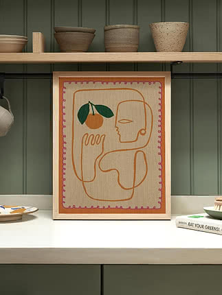 Art textile abstrait encadré avec visage, main et orange sur un plan de cuisine
