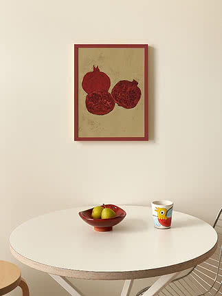 Affiche encadrée de grenades rouges au-dessus d’une table blanche avec coupe de fruits et tasse colorée