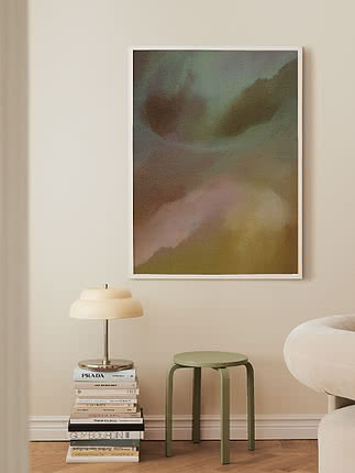 Affiche d’art abstrait en cadre blanc au-dessus d’un tabouret vert et d’une lampe de table