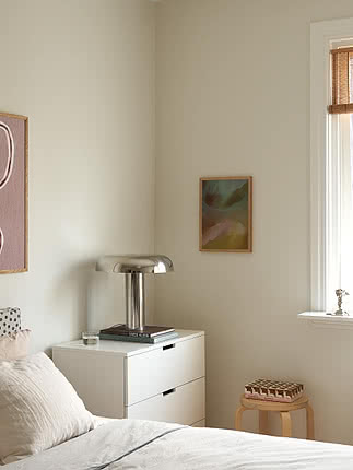 Coin de chambre avec commode blanche, lampe chromée, art mural et tabouret en bois