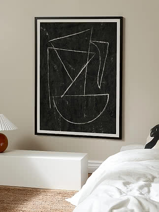 Indrammet abstrakt plakat med hvide geometriske streger på sort baggrund over en seng