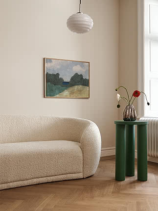 Green round side table beside a cream sofa with vase, flowers and wall art