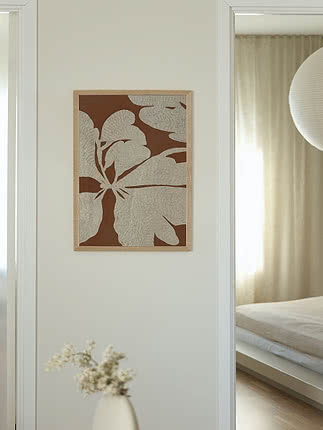 Framed botanical wall art with beige flower motif on a brown background in a bright room