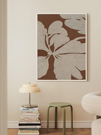 Framed botanical art print in brown and beige on wall above books, lamp and green stool