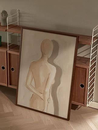 Abstrakt målning av en stående figur i träram, lutad mot en valnötsfärgad hylla.