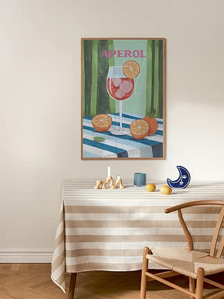 Inramad Aperol-affisch ovanför randigt bord med citroner och blå måndekor