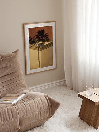 Poster incorniciato con ombre di palme su edificio dai toni caldi, appeso alla parete