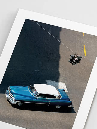 Overhead photo of a blue vintage car near a hanging traffic light on a sunlit street