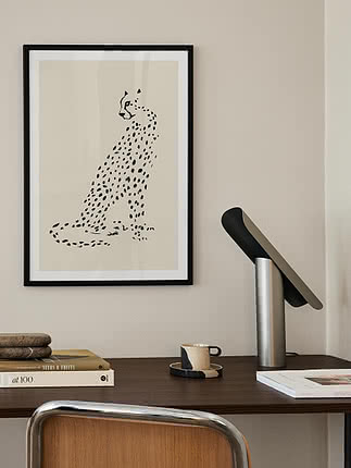 Poster incorniciato con illustrazione minimalista di un ghepardo nero su sfondo chiaro sopra una scrivania.