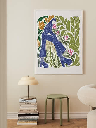 Stampa artistica colorata incorniciata con figura seduta tra grandi foglie e fiori su parete beige