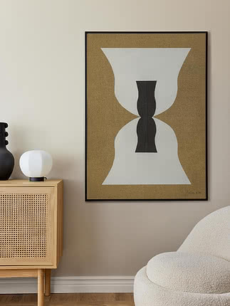 Abstrakt plakat i sort ramme over en rattan-kommode med bordlampe