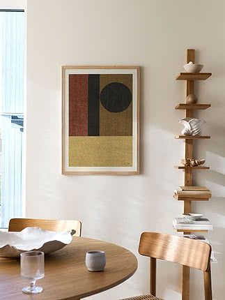 Indrammet geometrisk plakat over et rundt egetræsbord ved siden af en hylde med keramik