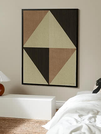 Geometrisk plakat i sort ramme over en hvid bænk i et soveværelse