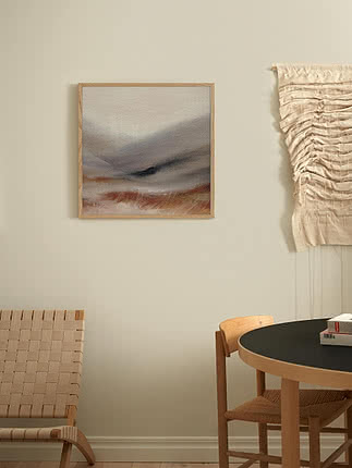 Stampa Faded Field in cornice di rovere su parete greige, accanto a un macramè crema appeso e a una sedia in pelle cuoio