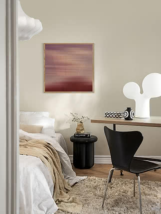 Stampa Claret in cornice di rovere su parete beige in camera, sopra un tavolino rotondo nero accanto a un letto in lino