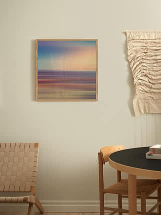 Stampa Prism Sky in cornice di rovere su parete greige, accanto a un macramè crema appeso e a un tavolo rotondo nero