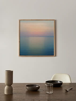 Stampa Hazed Dawn in cornice di rovere su parete chiara, sopra un tavolo in legno scuro con un vaso di pietra e ciotole