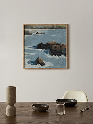 Stampa Cliff View in cornice di rovere su parete chiara, sopra un tavolo in legno scuro con un vaso di pietra e ciotole