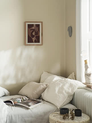 Trykket Maroon i egeramme højt på en beige væg over en daybed med hvide hørpuder og et stenbord ved siden af