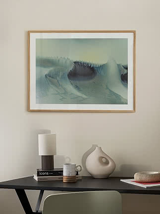 Trykket Icy Dune i egeramme på en beige væg over et sort skrivebord med lampe, en bleg vase og en grøn stol