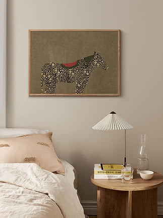 Trykket Whimsical Horse i egeramme på en beige væg over en seng med en rosa pude og et rundt træsidebord