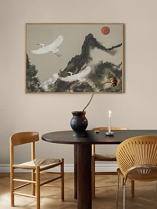 Trykket Egret Flight i egeramme på en beige væg over et mørkt rundt spisebord med en vase og et tændt lys